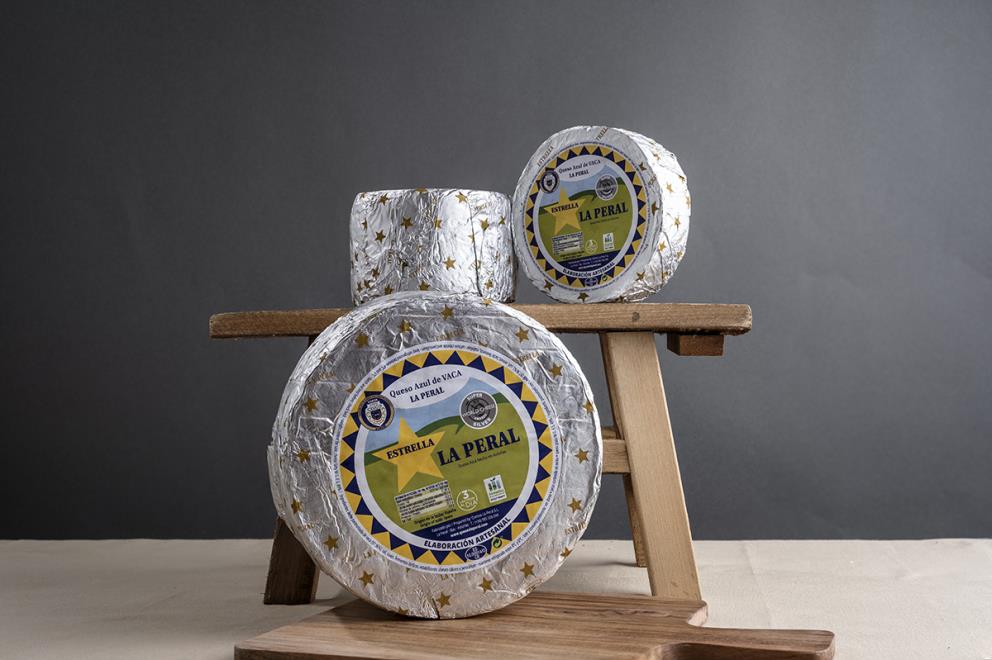 The three sizes of Estrella La Peral blue cheese on a wooden bench, highlighting its characteristic silver wrapper with gold stars.